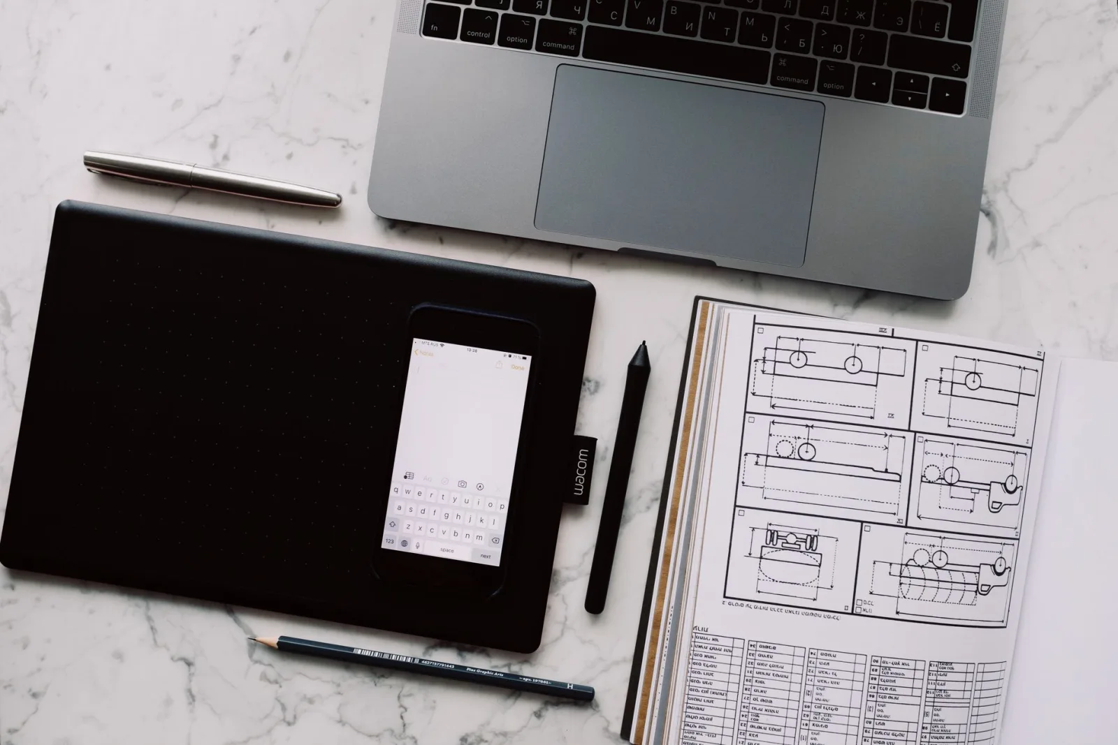 Designer drafting sketches on graph paper with smartphone and pencils on a wooden desk.
